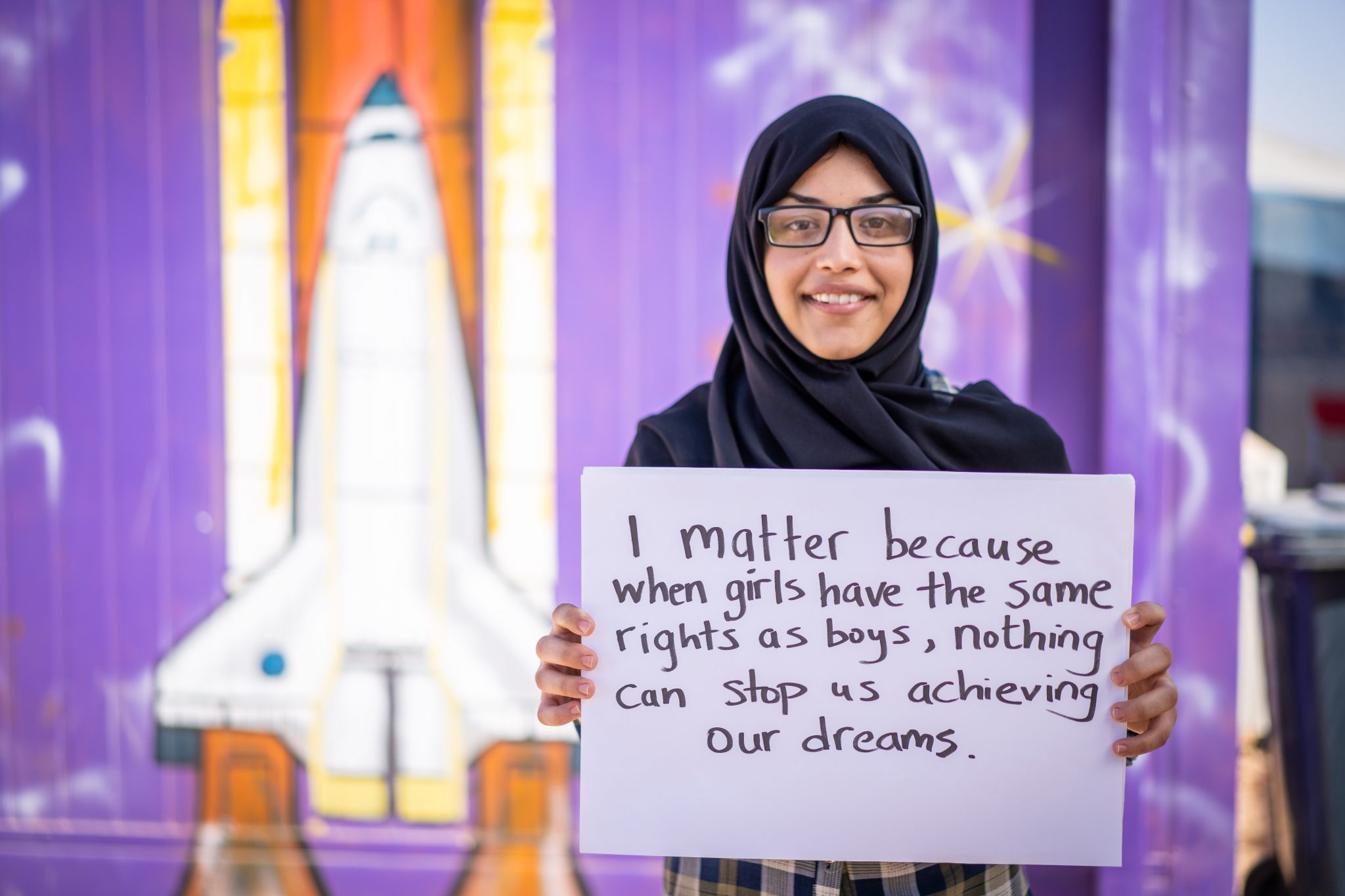 Young woman standing and holding a sign in front of a purple wall